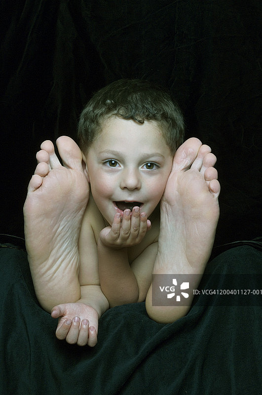 男孩(2-4)躺在父亲两脚之间，手托下巴，面带微笑图片素材