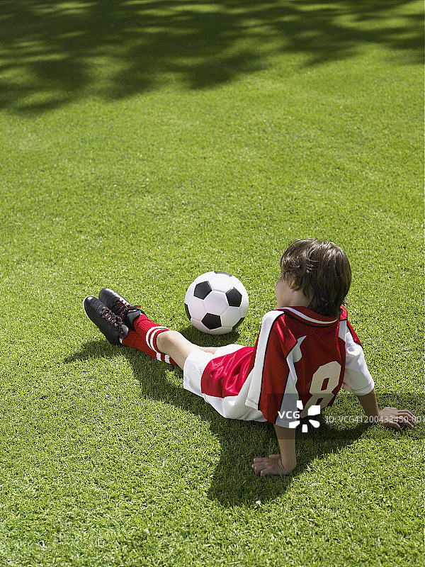 男孩(6-8)坐在草地上踢足球，后视镜图片素材