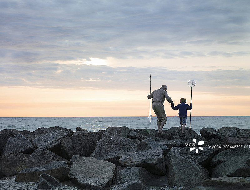 祖父和孙子(4-6岁)带着钓鱼设备在岩石上行走图片素材