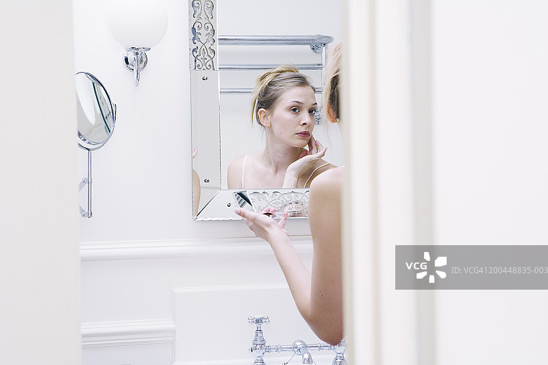 年轻女子看着浴室的镜子(专注于反射)图片素材