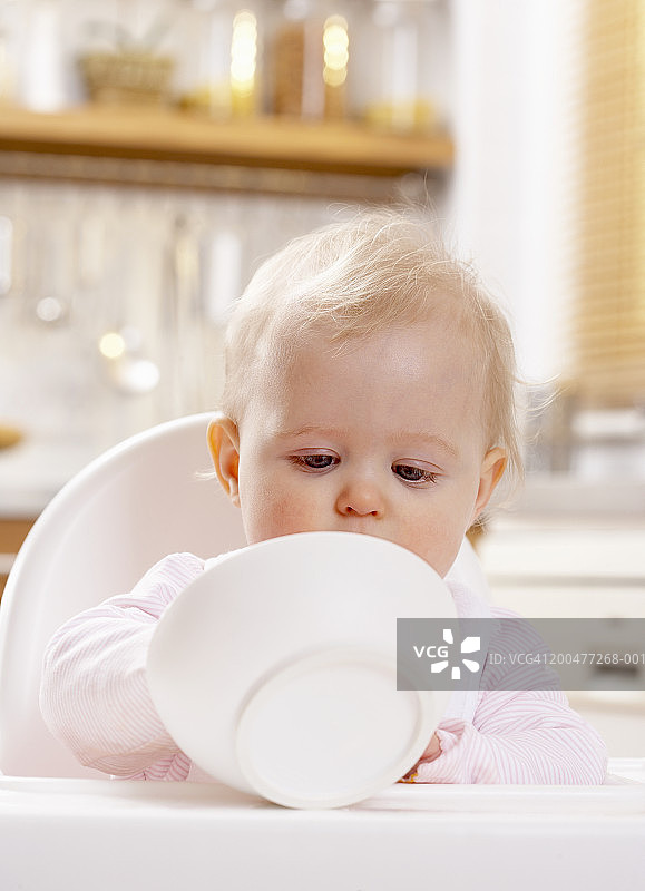 女婴(8-10个月)坐在高椅子上，端着碗图片素材