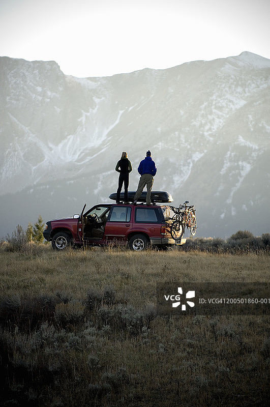 年轻夫妇站在SUV车顶，看山景，看后景图片素材