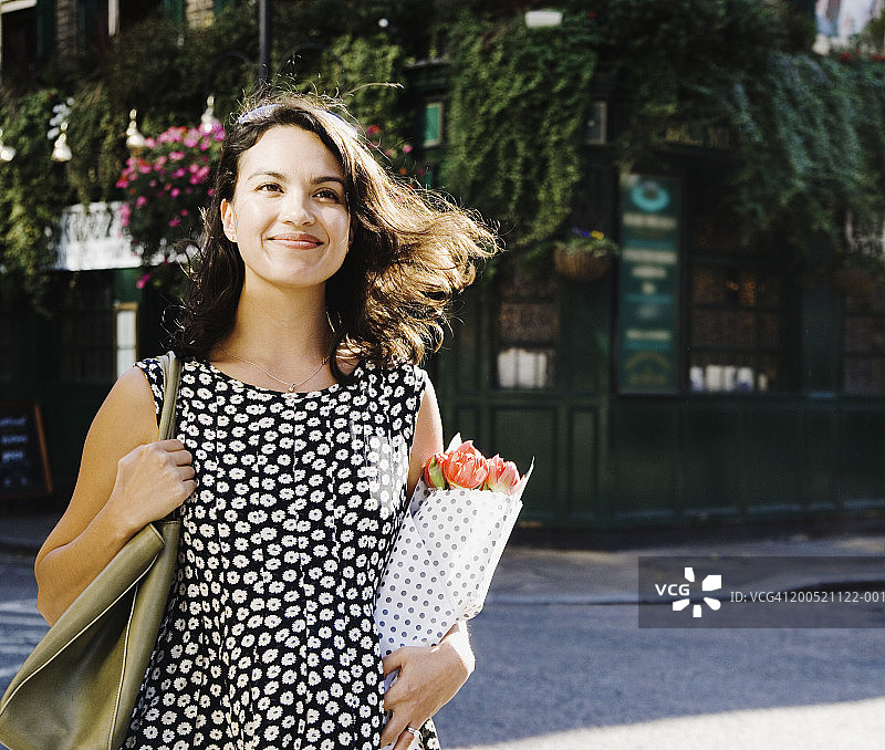 女人站在街上，手里拿着一束鲜花，面带微笑图片素材