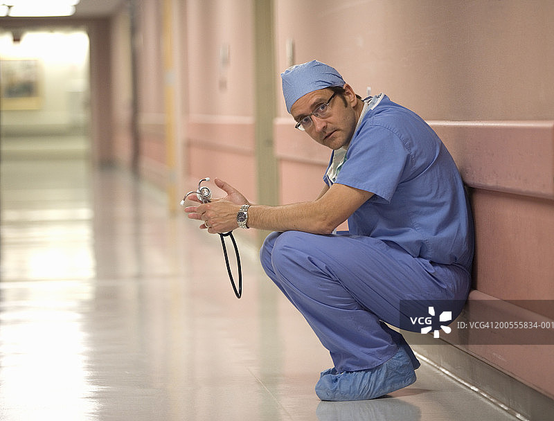 穿着手术服的外科医生，在医院走廊里靠墙蹲着图片素材