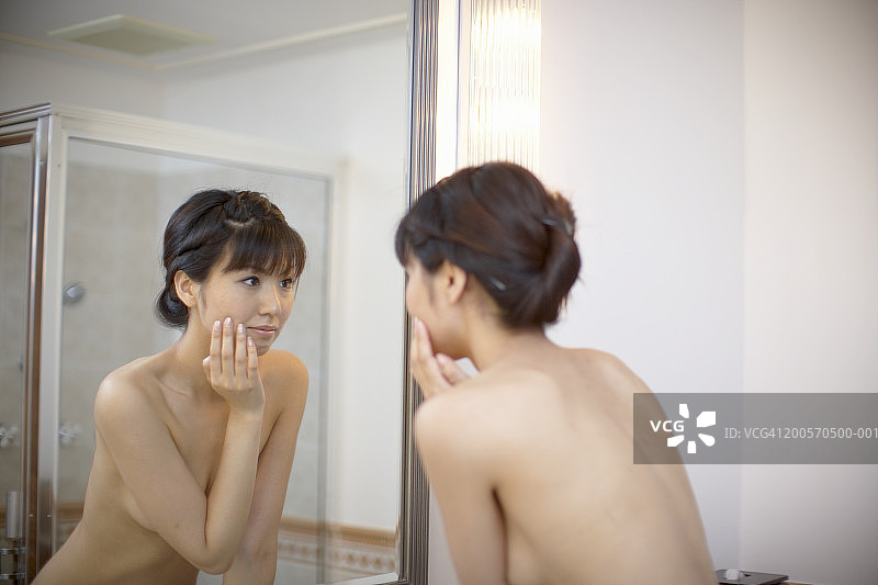 年轻女子看着浴室里的镜子，特写镜头图片素材