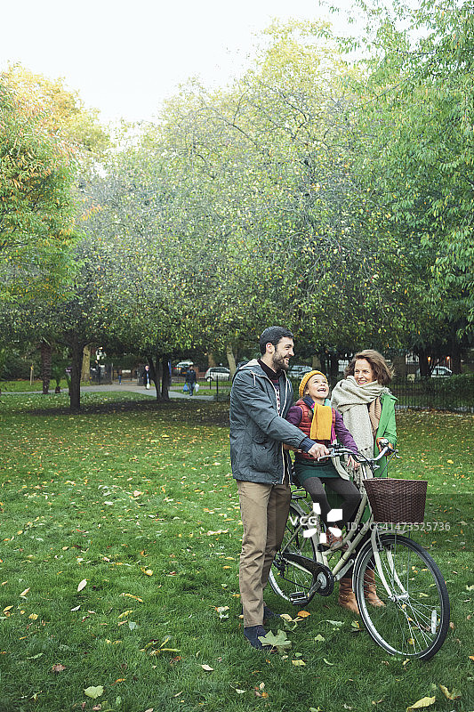 小女孩和爸爸、奶奶在公园里骑自行车。图片素材