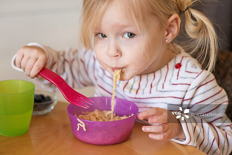蹒跚学步的小女孩正在吃碗里的面条图片素材
