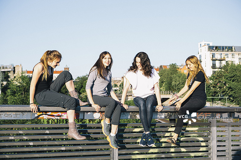 城市生活:女性朋友一起坐在栏杆上图片素材