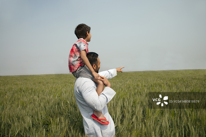 一名印度男子背着儿子指着天空中的农场图片素材