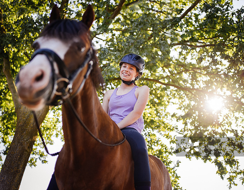 女孩骑着她的马在郁郁葱葱的绿树下图片素材
