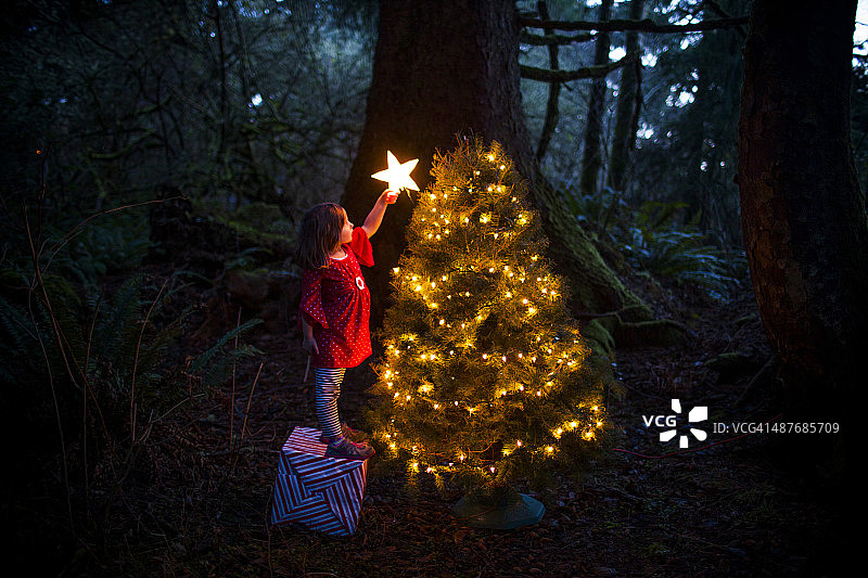 一个高加索女孩在森林里装饰圣诞树图片素材