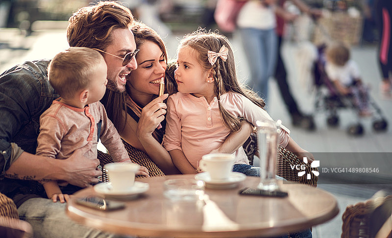 微笑的父母和他们的小孩在咖啡馆享受。图片素材