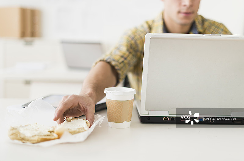 美国新泽西州泽西城，一个年轻人一边吃着三明治一边用着笔记本电脑图片素材