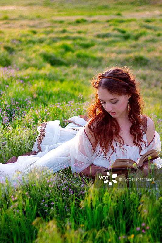 拿着书的女人闭着眼睛坐在草地上图片素材