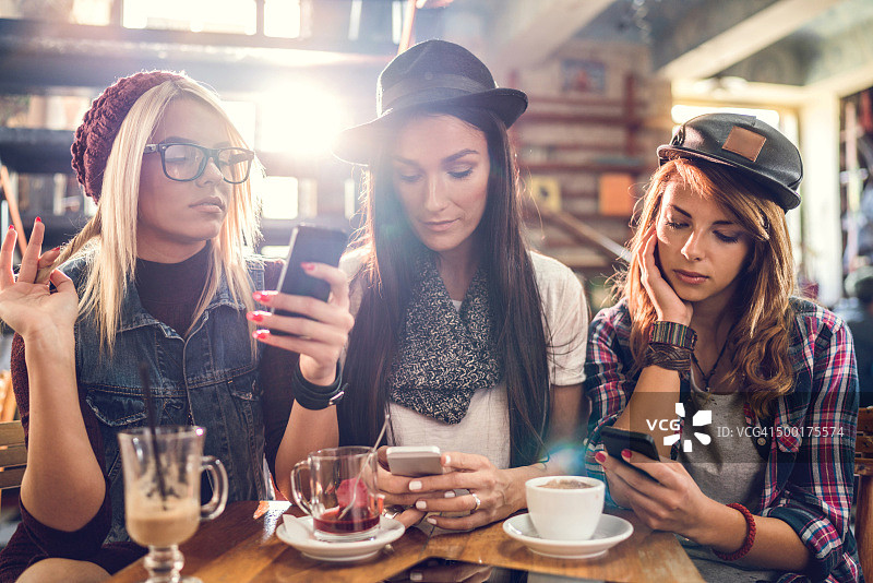 三个女人在咖啡馆用她们的智能手机。图片素材