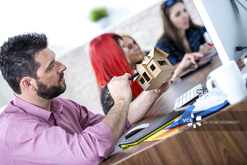男建筑师在电脑前，手里拿着一个模型房子图片素材