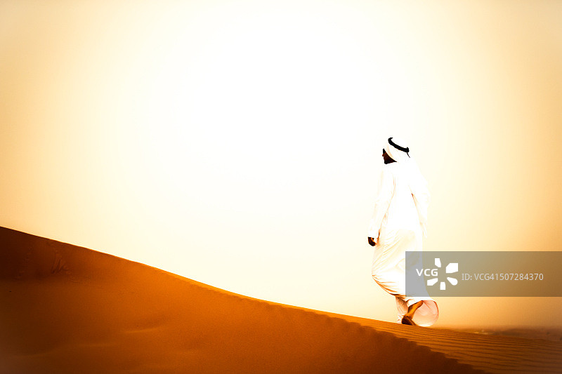 在一个炎热的夏天，一个阿拉伯人在沙丘上行走图片素材