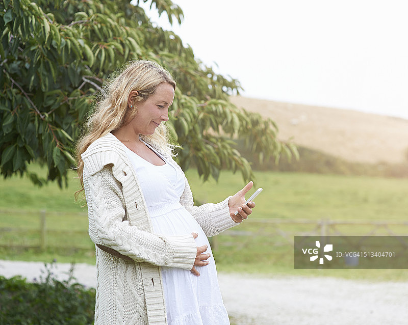 孕妇使用手机在农场的概况。图片素材