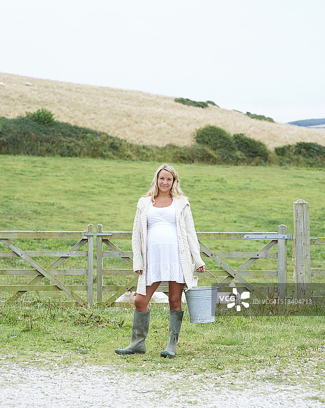 一个孕妇带着水桶站在农场里。图片素材