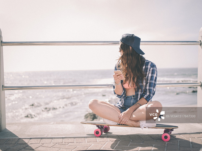 海滩上坐在滑板上的嬉皮士女孩图片素材