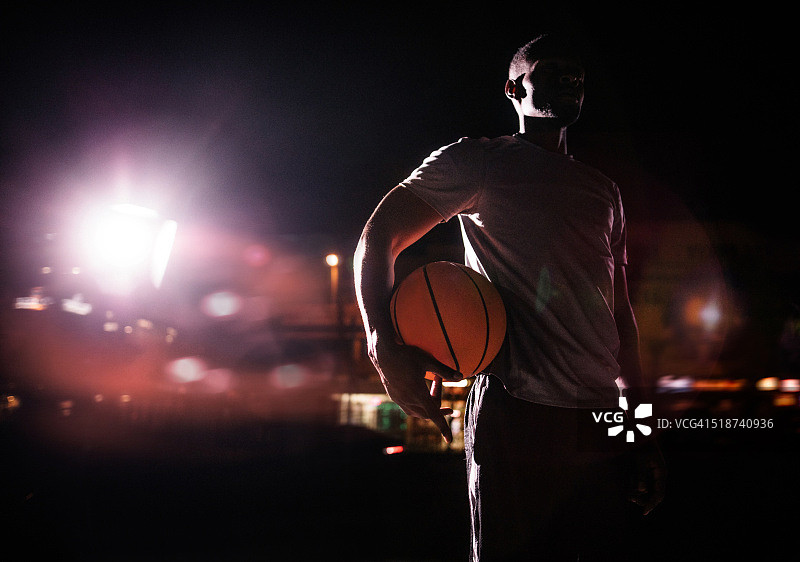 男子篮球运动员抱球在臀部在晚上图片素材