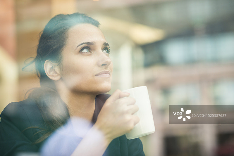 年轻的女商人喝咖啡，看着窗外，伦敦，英国图片素材