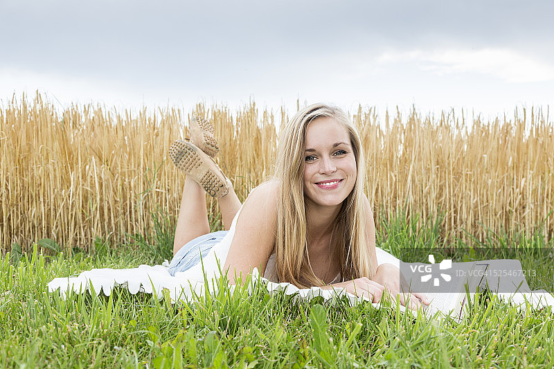 一个微笑的年轻女子躺在黑麦前的毯子上的肖像图片素材