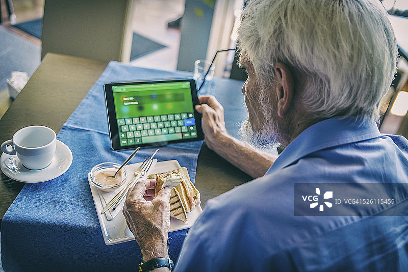 老人们吃着早餐，用着平板电脑。图片素材