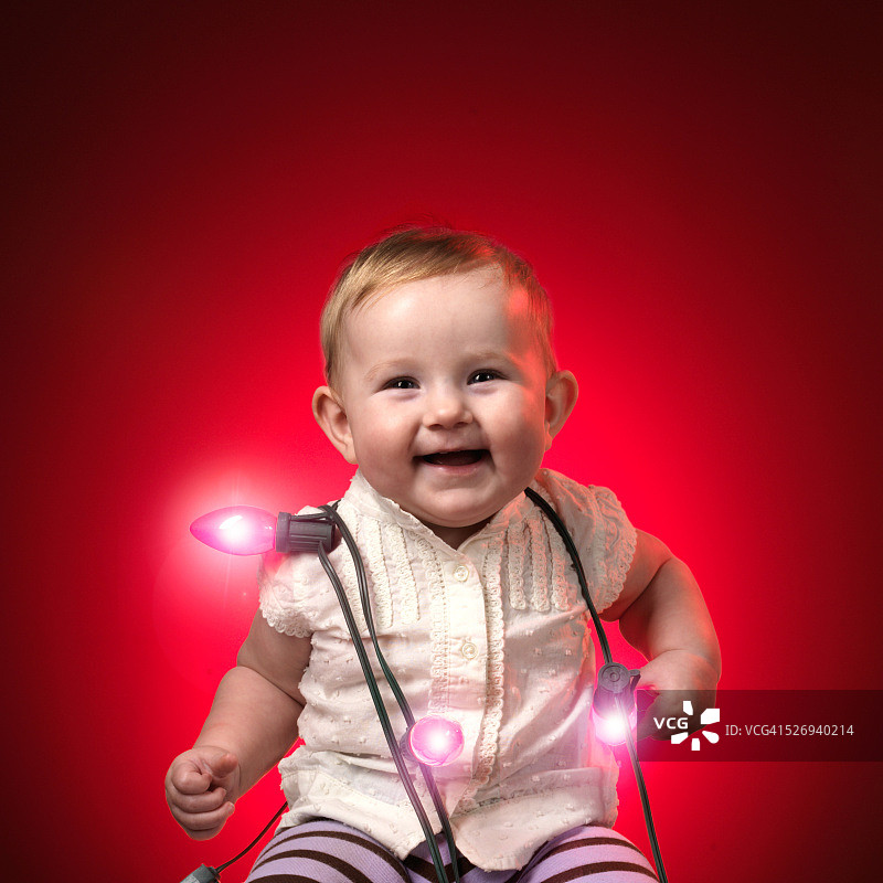 微笑的婴儿包裹在红色的圣诞灯图片素材