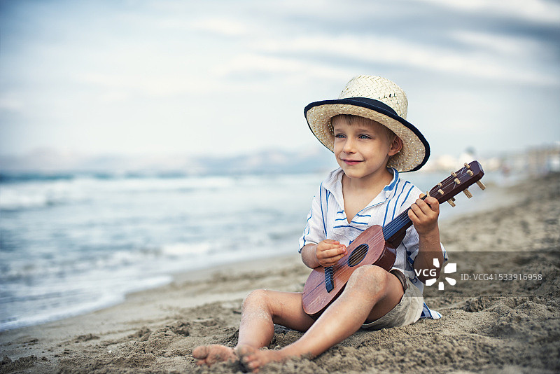小男孩在沙滩上弹吉他。图片素材