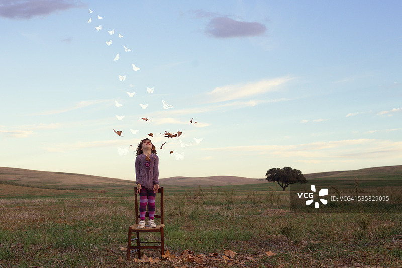 女孩站在椅子上，抬头看着秋叶变成蝴蝶图片素材
