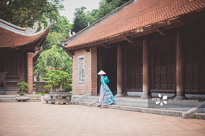 越南河内，一名身穿传统服饰的女子走进一座木制寺庙图片素材