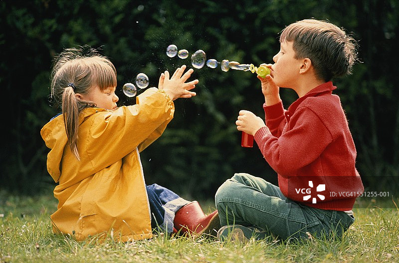 男孩和女孩[3-4]，坐在花园里，男孩对着女孩吹泡泡图片素材