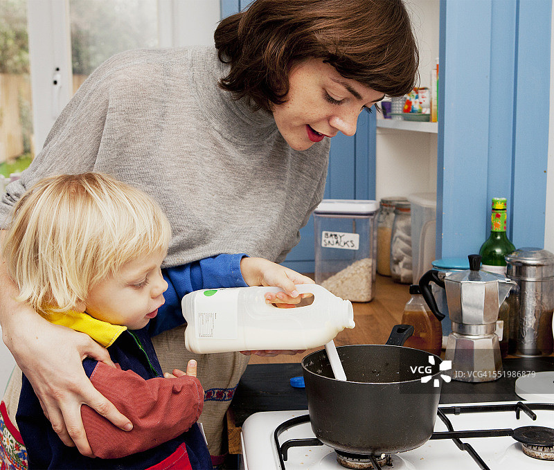 母亲和儿子在厨房的粥锅里倒牛奶图片素材