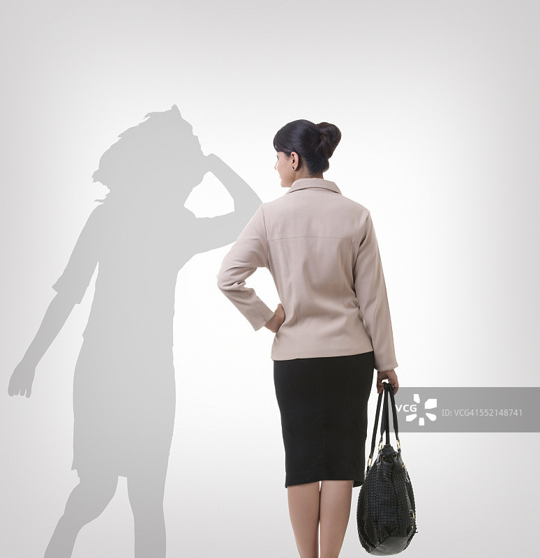 后视图的女商人看她的影子跳舞在灰色的背景图片素材