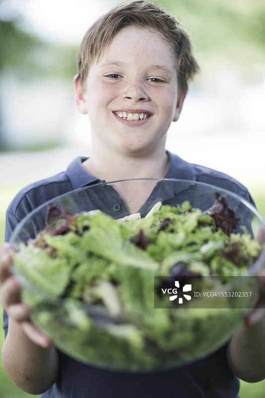 一个微笑的男孩拿着一碗沙拉的肖像图片素材