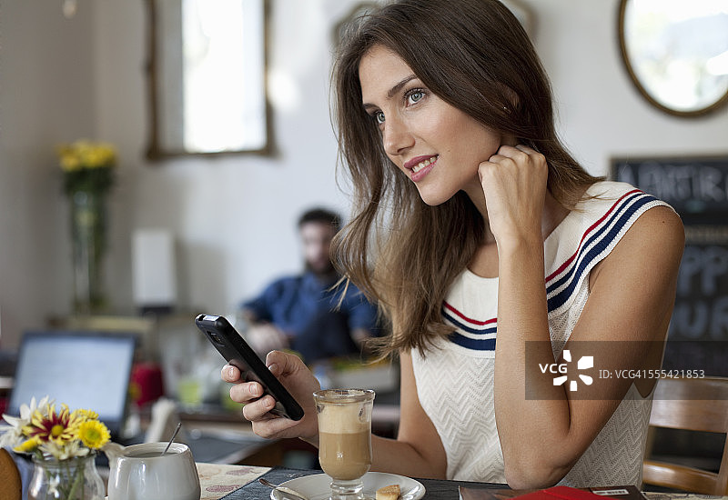 女人在café，喝着咖啡，用着智能手机图片素材