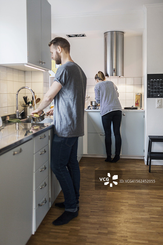 男人在洗平底锅，女人站在厨房的后面图片素材
