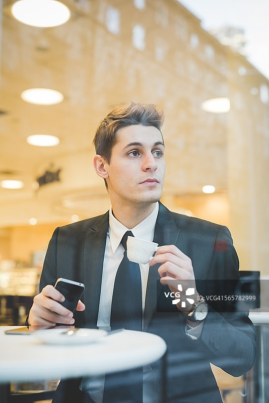 年轻的商人坐在咖啡馆使用平板电脑和手机的肖像。图片素材