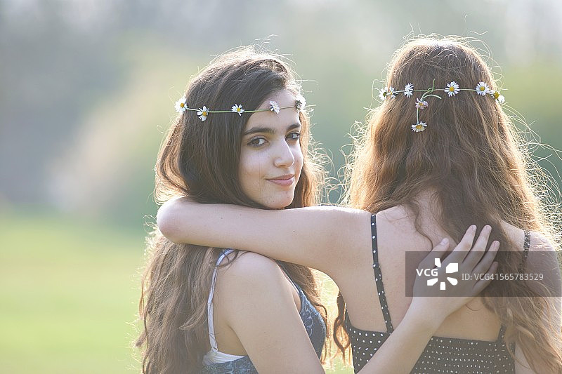 两个十几岁的女孩在公园戴着雏菊链头饰的后视图肖像图片素材