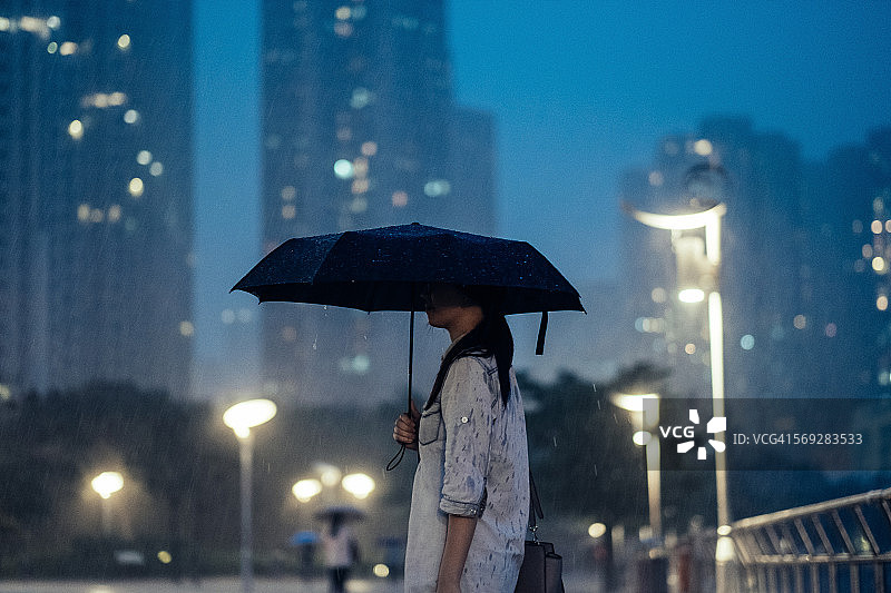 女人撑着雨伞在倾盆大雨中穿行在城市街道上图片素材