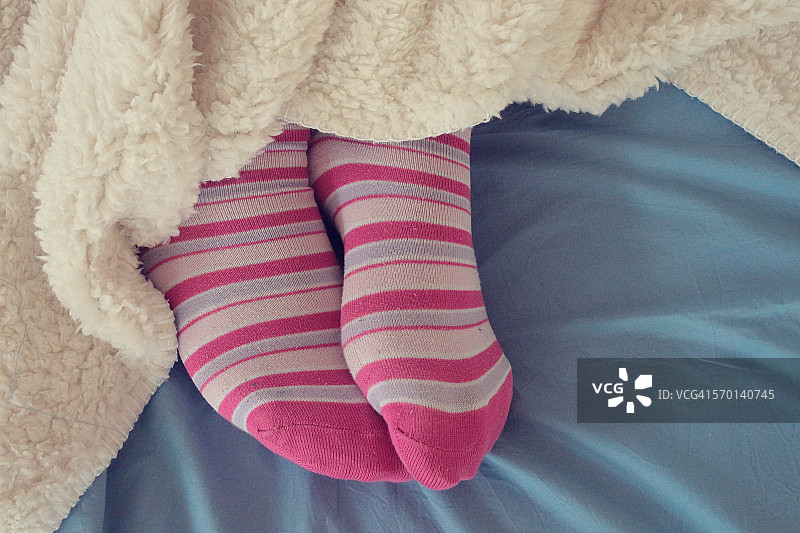 穿粉红袜子的女人的脚从毯子下面伸出来图片素材