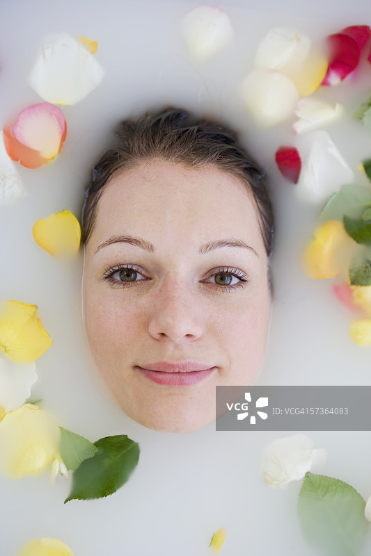 年轻女子的脸在洗澡水和周围的玫瑰花瓣图片素材