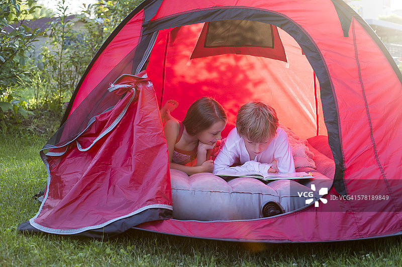 男孩和女孩躺在一个红色的帐篷里看书图片素材