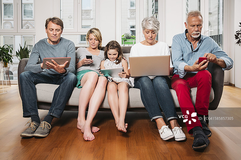 三代同堂的家庭坐在一个沙发上使用不同的数码设备图片素材
