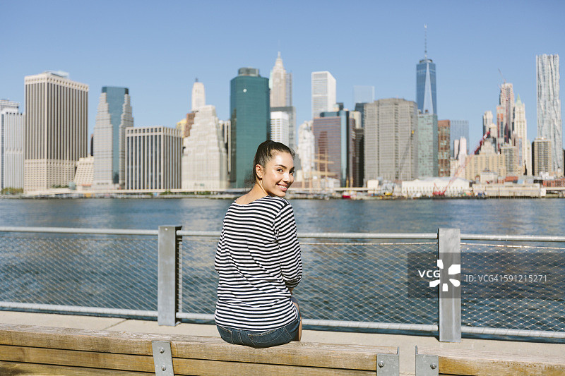 美国，纽约市，年轻女子坐在天际线前，从她的肩膀上看图片素材