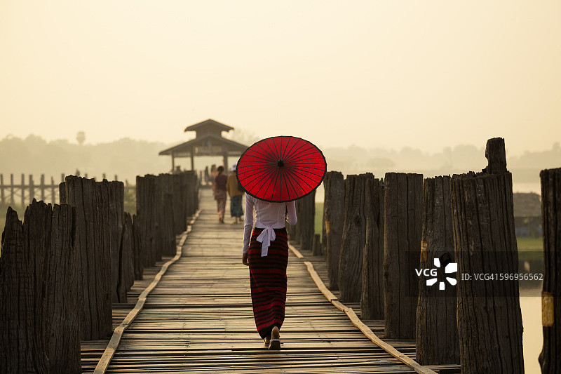 缅甸早上的妇女拿着红伞在U拜因桥上图片素材