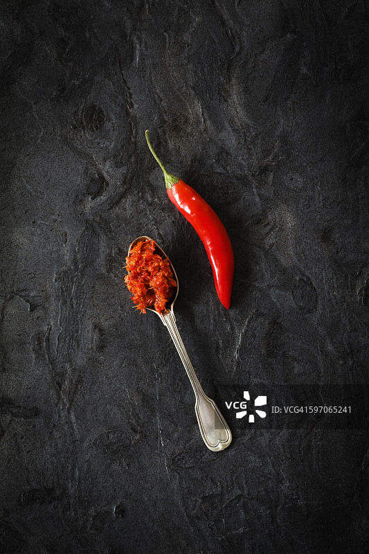 一勺自制的辣椒酱和辣椒荚放在黑色的地面上图片素材