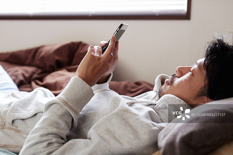 年轻人躺在床上玩手机图片素材