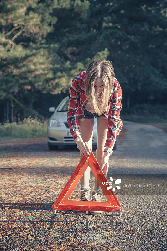一名年轻女子因车辆故障在乡村车道上设置了三角形警告图片素材